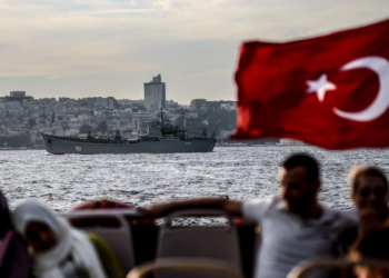 Uma bandeira turca tremula em um navio mercante turco, enquanto um navio de guerra russo cruza o Bósfor em rota ao Mediterrâneo
AFP/Getty